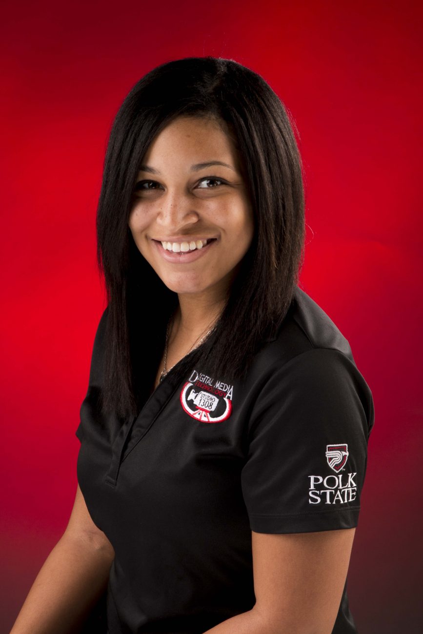 Portrait of Ashley Bramwell in the black Digital Media Studio 1308 shirt against a red backdrop