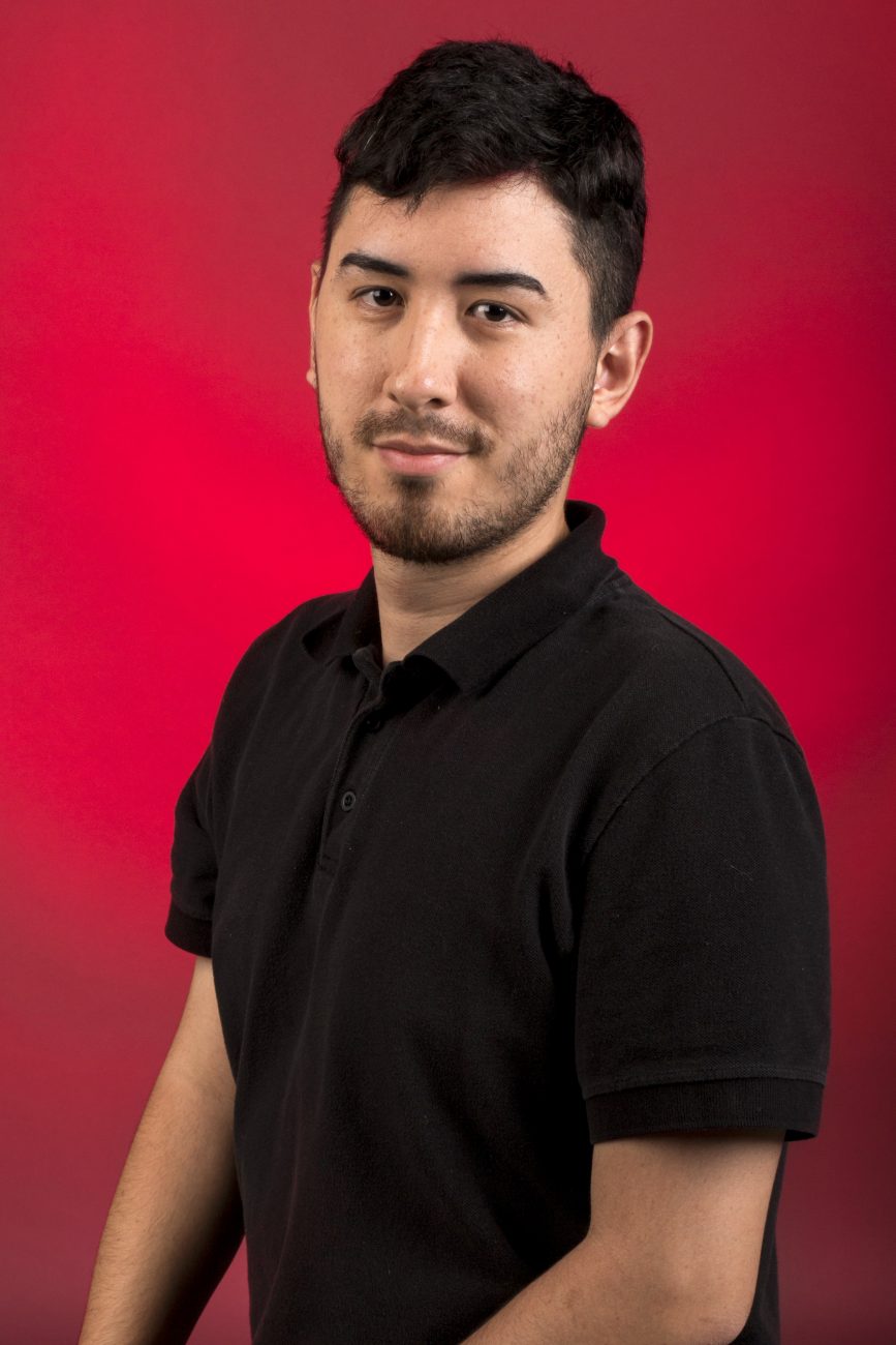 Portrait of Daniel Carrion Jr. in a black collared shirt against a red backdrop