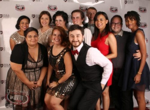 Digital Media staff and students pose against a logo patterned backdrop. 