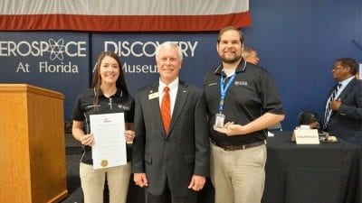 Polk State Aerospace student Karissa Strickland, left, Lakeland Mayor Howard Wiggs, center, and Polk State Aerospace Director Eric Crump. On Tuesday, Wiggs read a proclamation honoring Polk State Aerospace and other local organizations advancing aerospace education in Polk County. Strickland holds a copy of the proclamation. Crump holds an honorary city key.