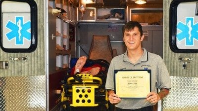 Polk State alumnus Jesse Stine stands with his Rookie of the Year certificate in front of the training ambulance used by Polk State's EMS Program.