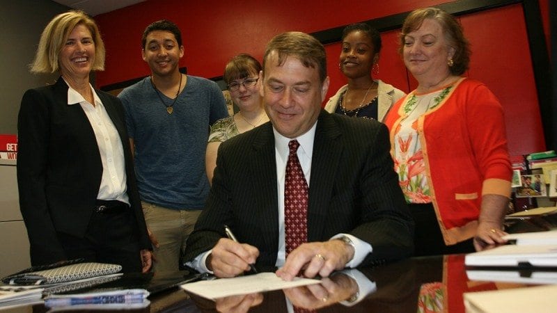 Winter Haven Economic Development Council Executive Director Bruce Lyon signs an agreement with Polk State that calls for increased collaboration on initiatives including internships, events and mentorships for students. Looking on are Julie Sands (L), program manager for the WHEDC, Bachelor of Applied Science Program Director Maria Lehcozky (R), and several students who attend Polk State Winter Haven.