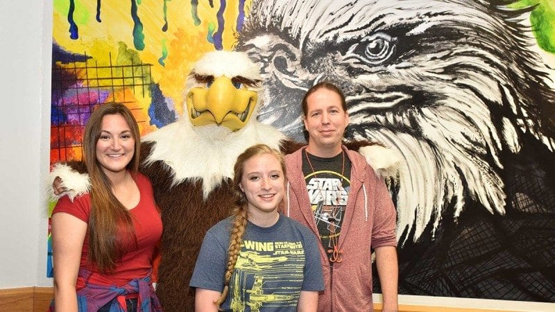 Amanda Frazier, left, designed the new mural in the Polk State Winter Haven game room. Her classmates, Kayla Wasmund, center, and Scott Whitley, right, helped paint it on the wall. On hand for Wednesday's mural reveal was Charlie, Polk State's mascot.